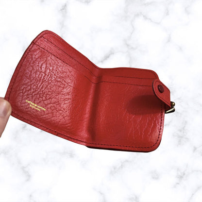 Red leather wallet held by a hand on a white marble background