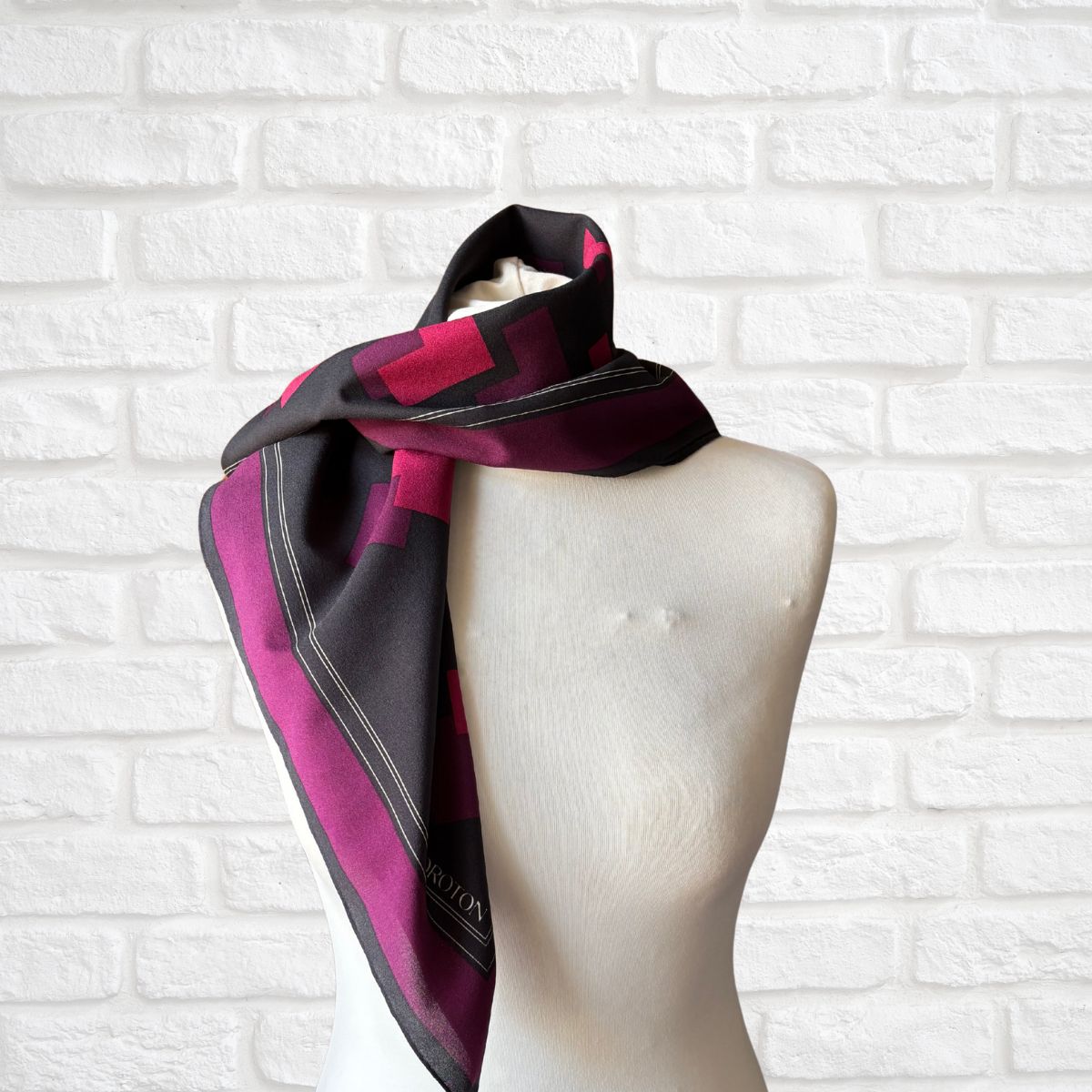Mannequin wearing a pink and black checkered scarf against a white brick wall.