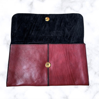 Two-tone black and red clutch bag with gold buttons on a white marble background