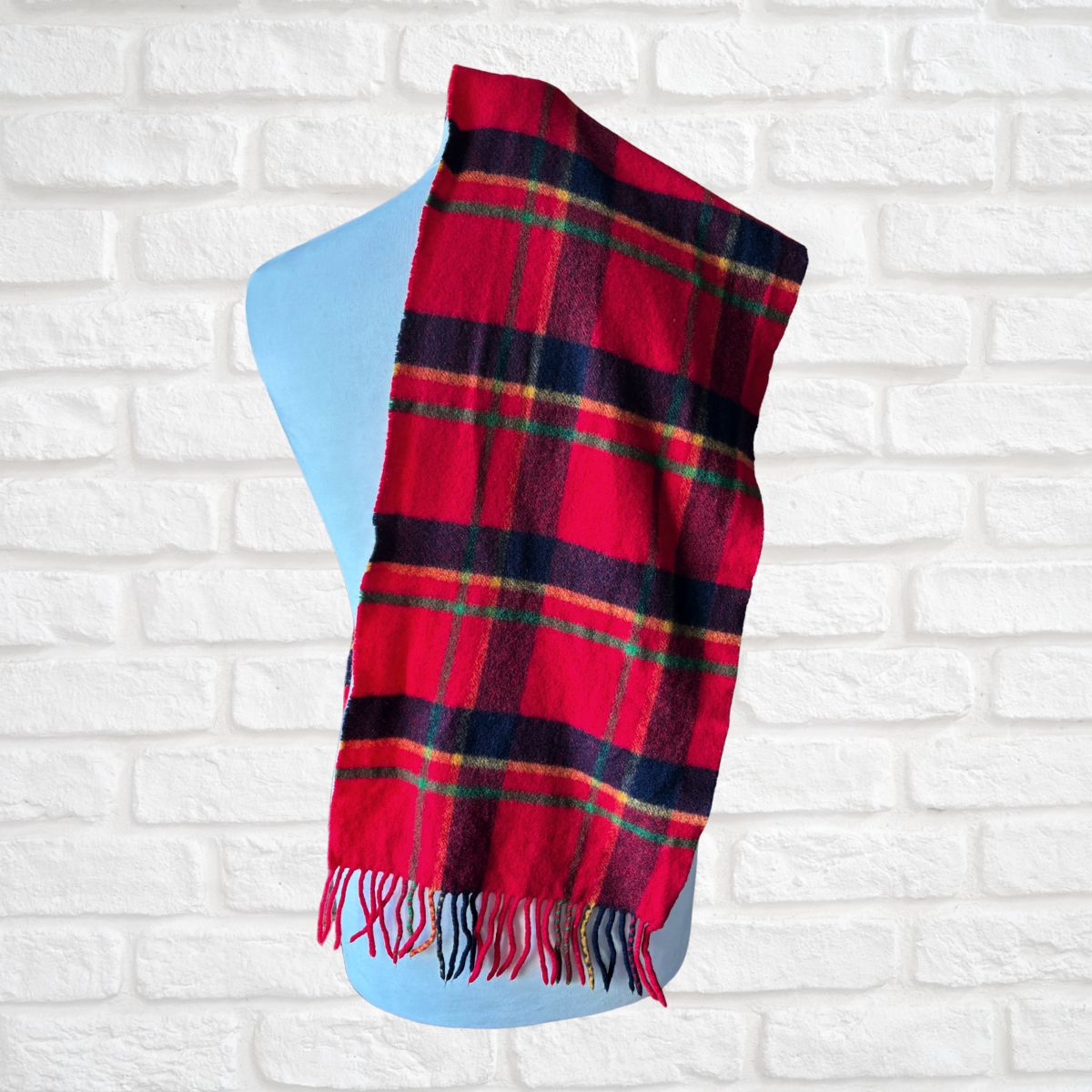 Red plaid scarf  on a blue stand against a white brick wall.