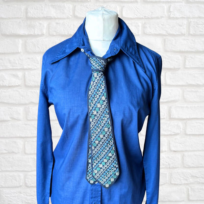 Blue shirt with a patterned tie on a mannequin against a white brick wall.