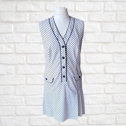 White sleeveless dress with blue polka dot pattern on a mannequin against a white brick wall.
