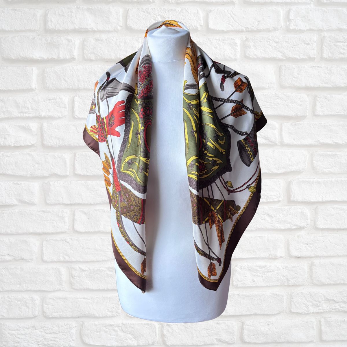 Decorative scarf with a pattern draped over a mannequin against a white brick wall.