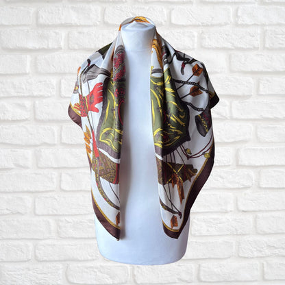 Decorative scarf with a pattern draped over a mannequin against a white brick wall.