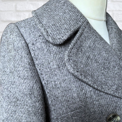 Close-up of a gray coat with a wide collar on a mannequin against a white brick wall.