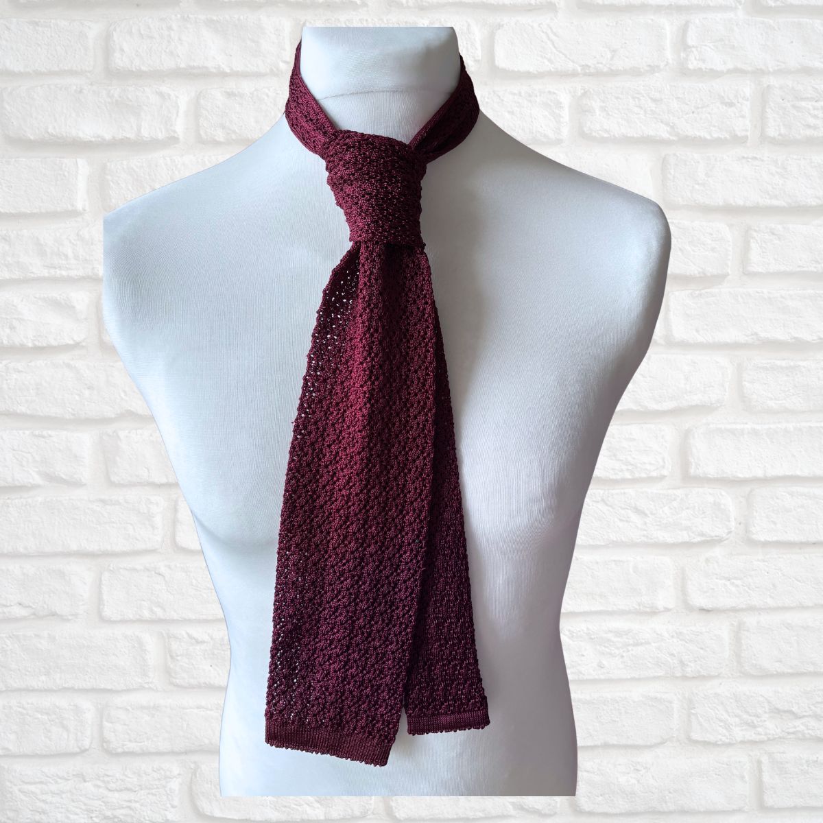 Maroon knitted scarf on a mannequin against a white brick wall background