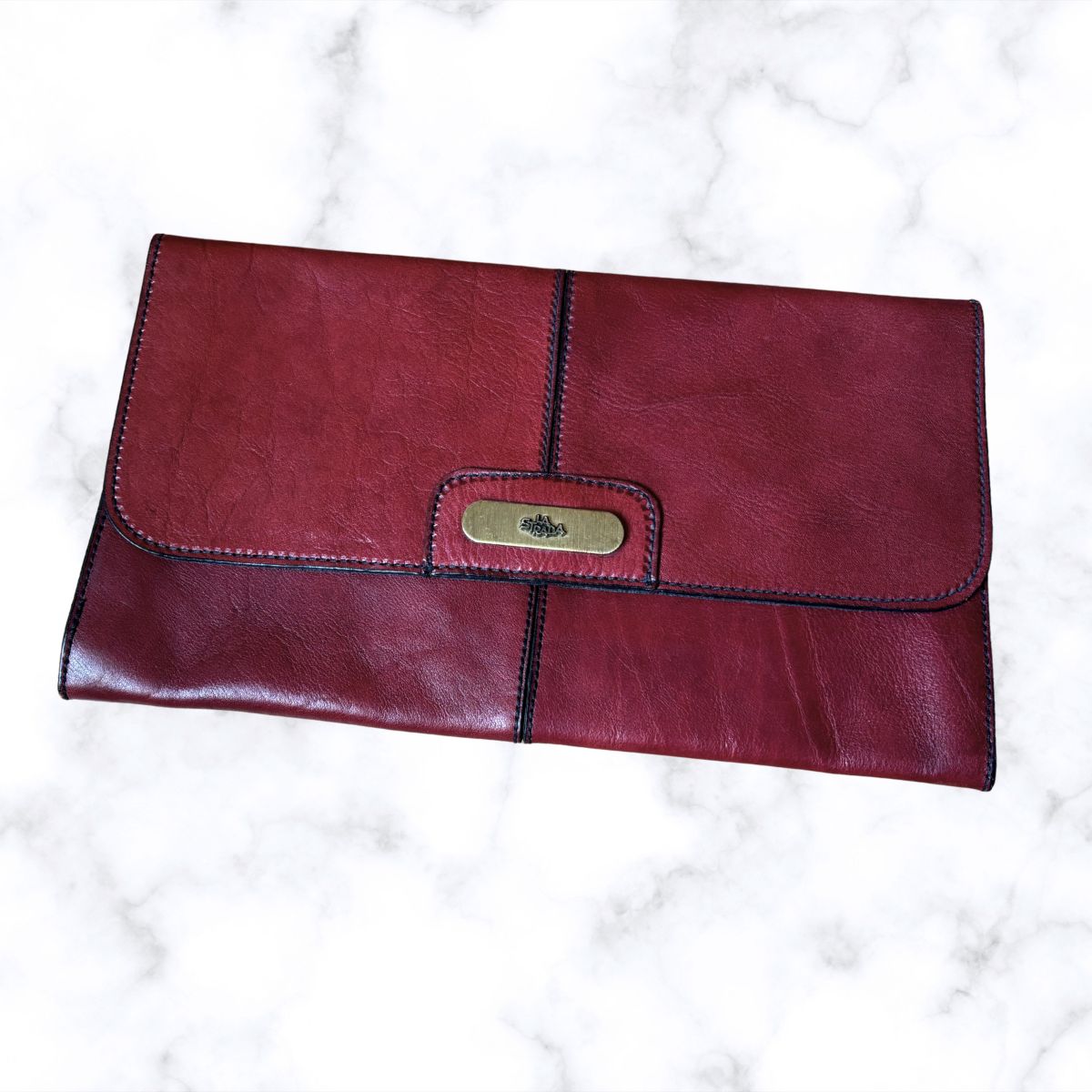 Red leather clutch bag with gold clasp on a white marble background