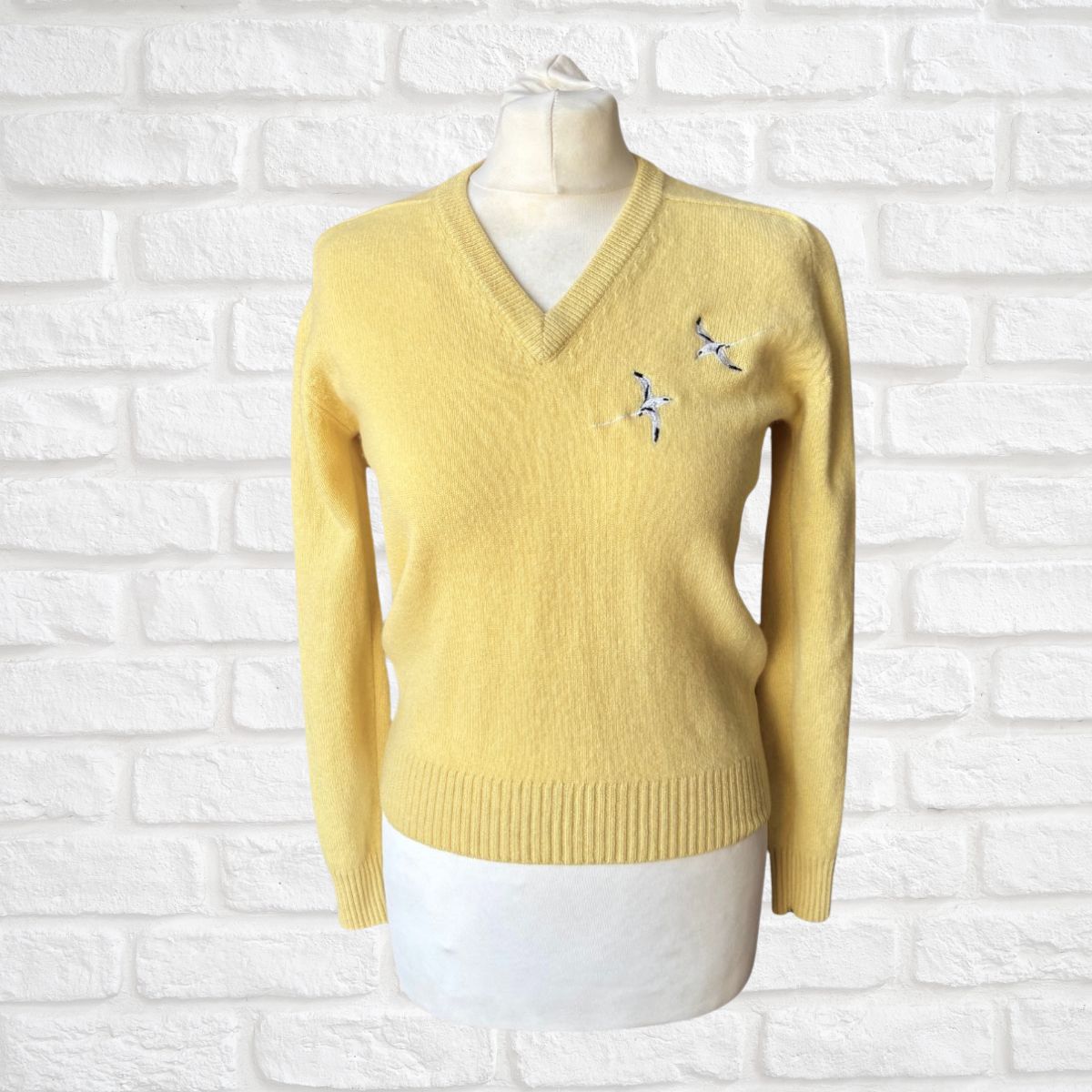 Yellow sweater with a bird motif on a mannequin against a white brick wall background