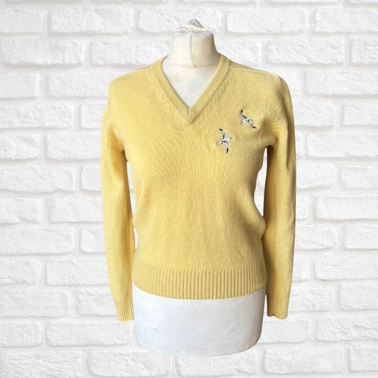 Yellow sweater with a bird motif on a mannequin against a white brick wall background