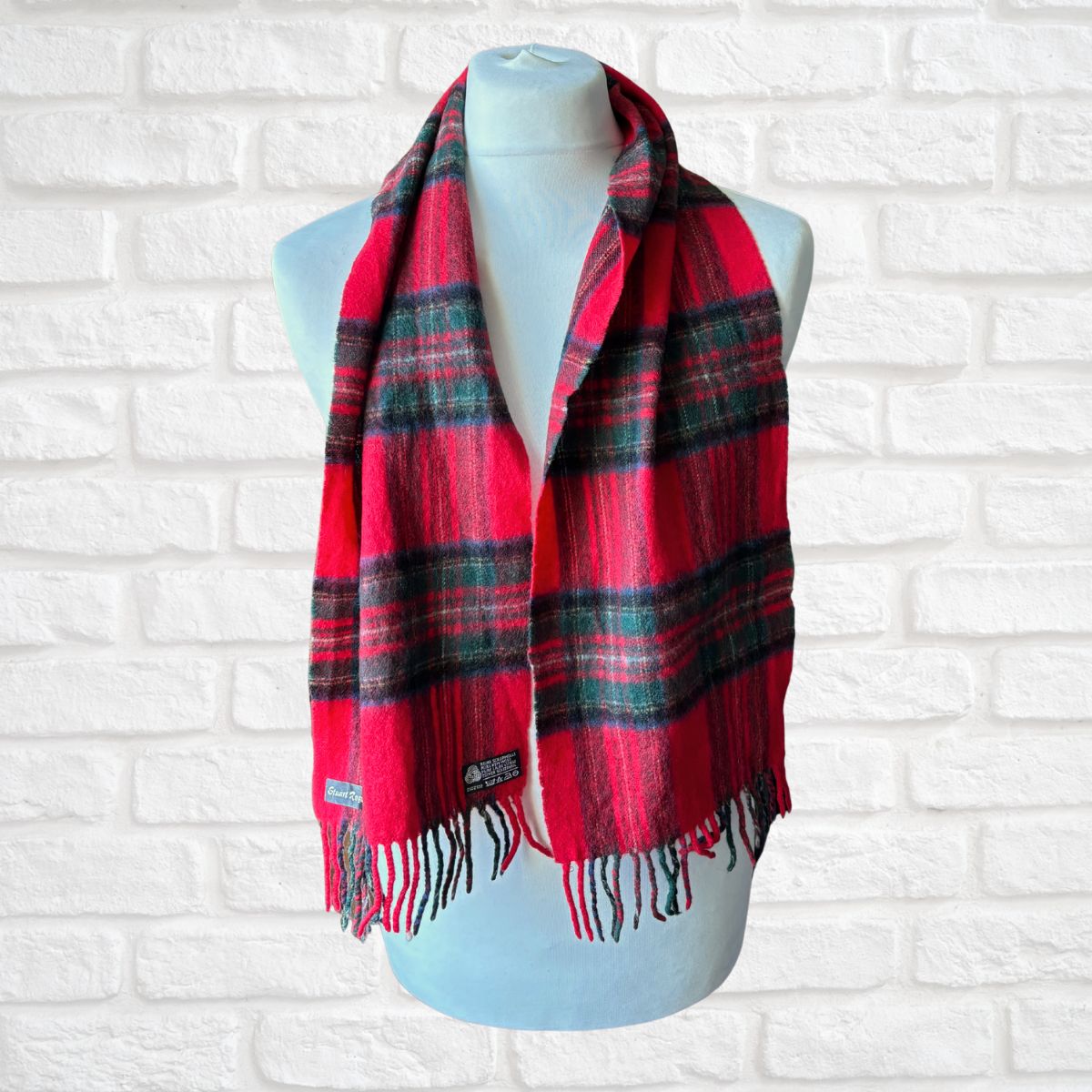 Red and black plaid scarf on a mannequin against a white brick wall.