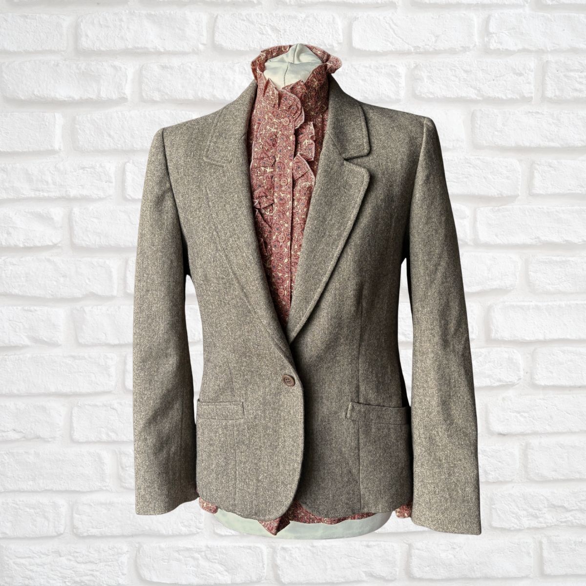 Neutral wool blazer with a patterned shirt on a white brick wall background