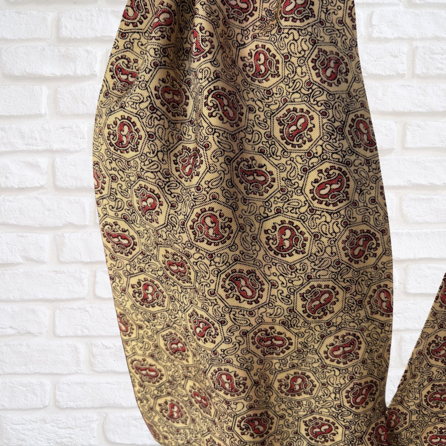 Patterned cravat with red and yellow  design on a white brick wall background
