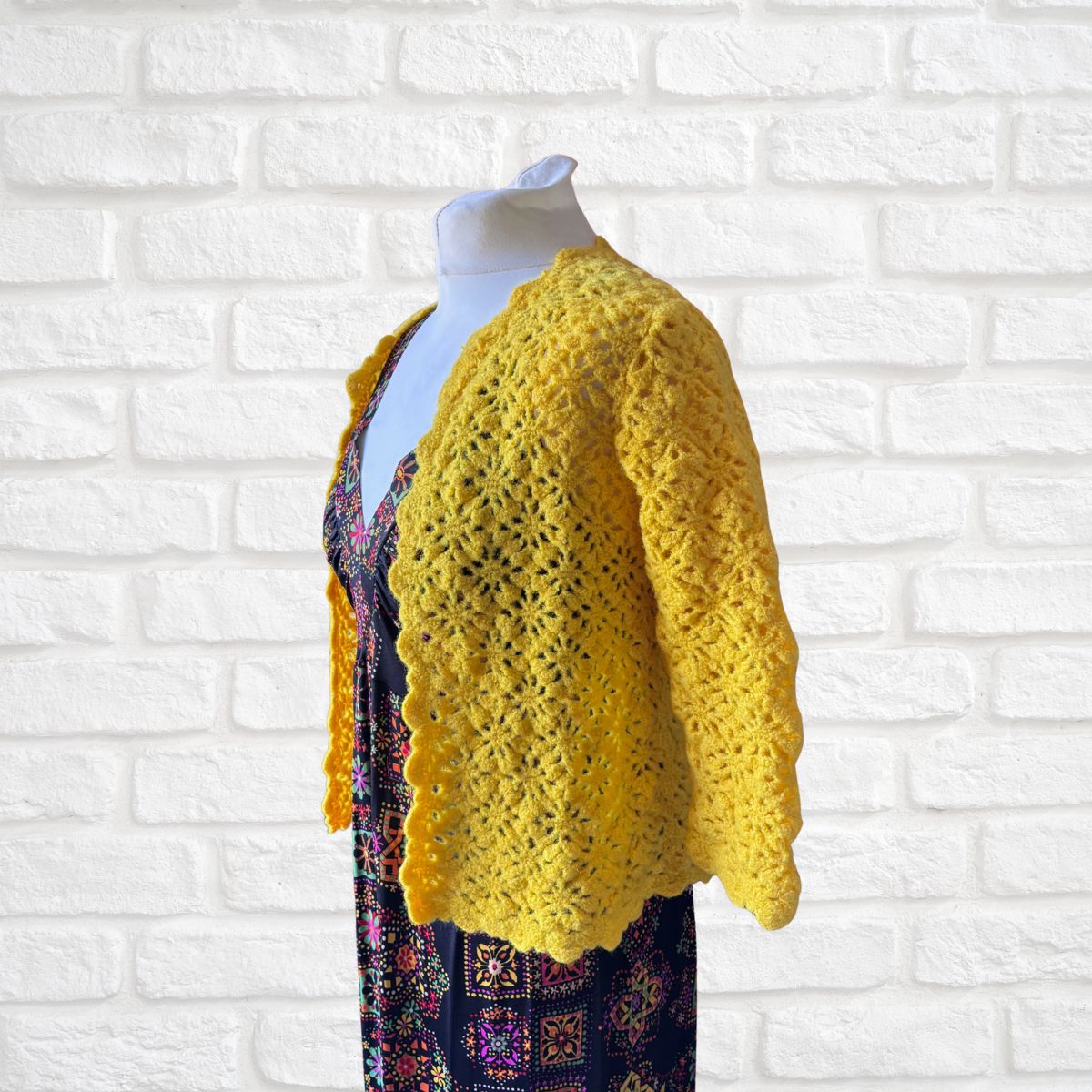 Yellow crocheted cardigan on a mannequin against a white brick wall background