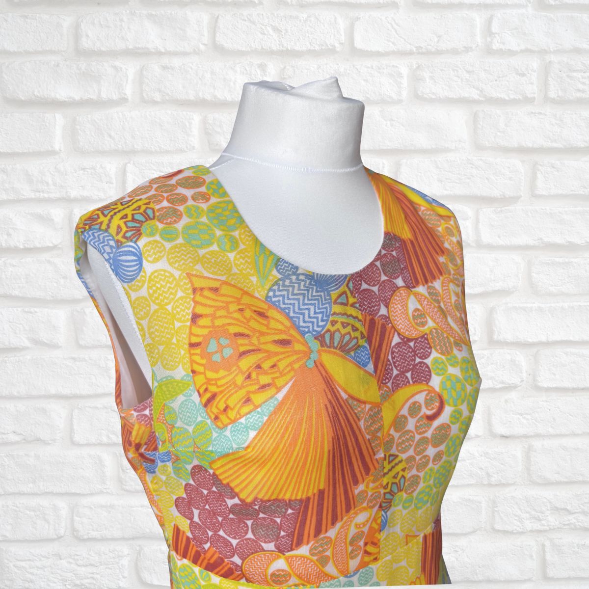 Colourful psychedelic -patterned dress on a mannequin against a white brick wall.