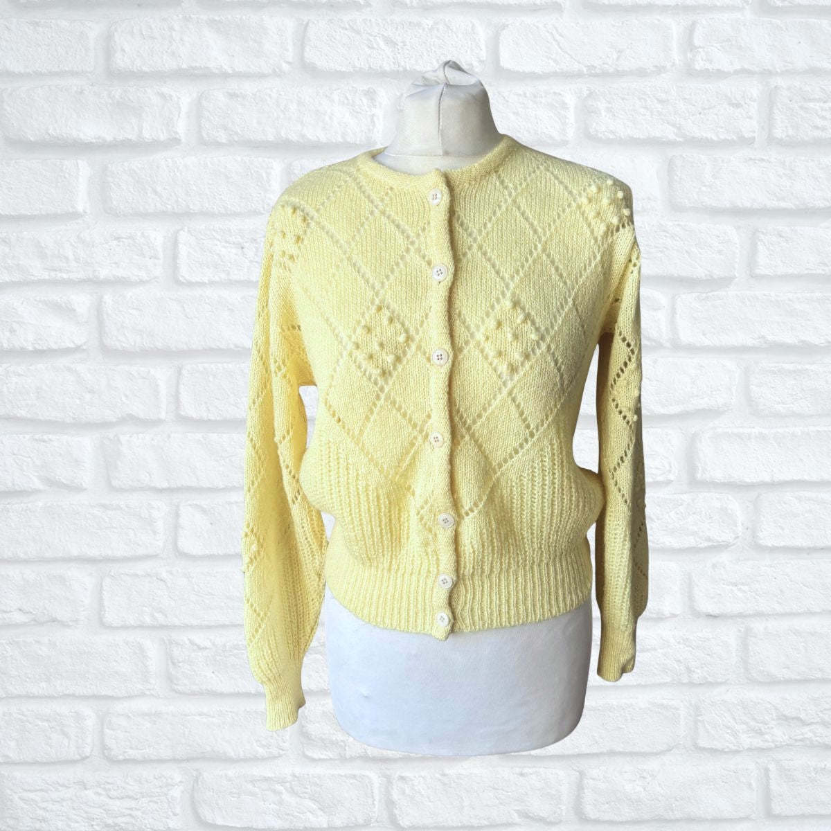 Yellow knitted cardigan on a mannequin against a white brick wall background