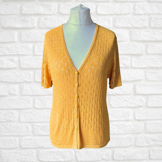 A yellow short-sleeve knit cardigan sweater with a V-neck and button-front closure, displayed on a mannequin torso against a white brick wall background.