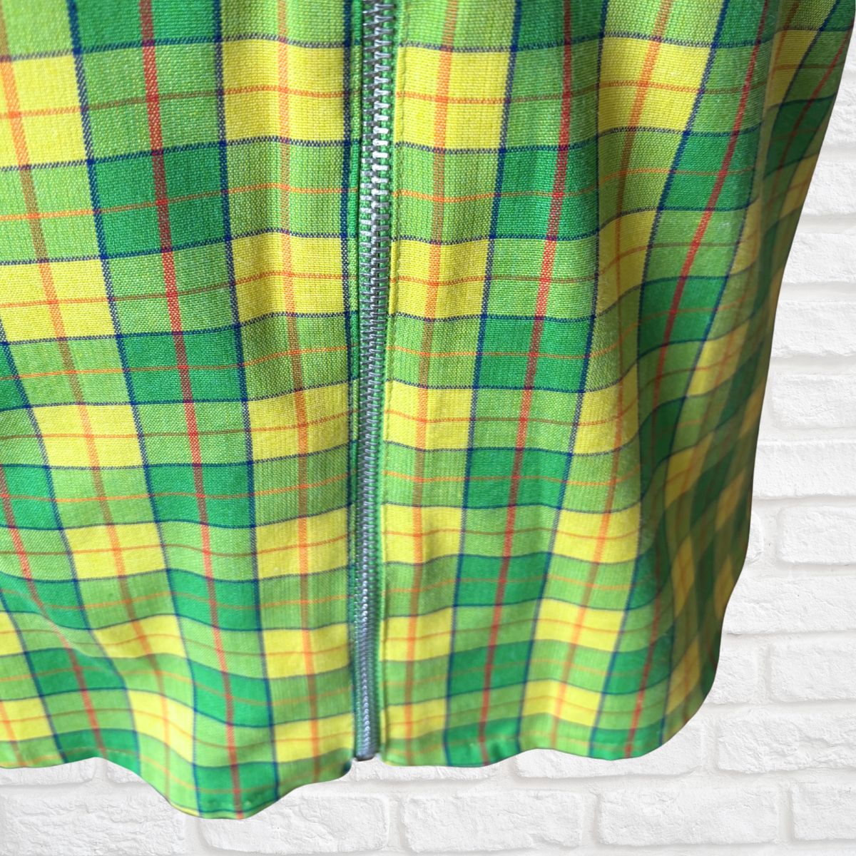 Green and yellow plaid fabric with a zipper on a white textured background