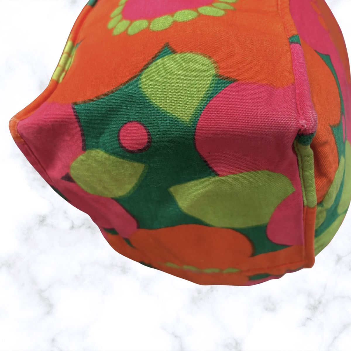 A close-up of a bag featuring a bold retro floral pattern in orange, pink, green, and yellow on a white marble surface.