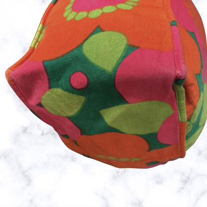 A close-up of a bag featuring a bold retro floral pattern in orange, pink, green, and yellow on a white marble surface.