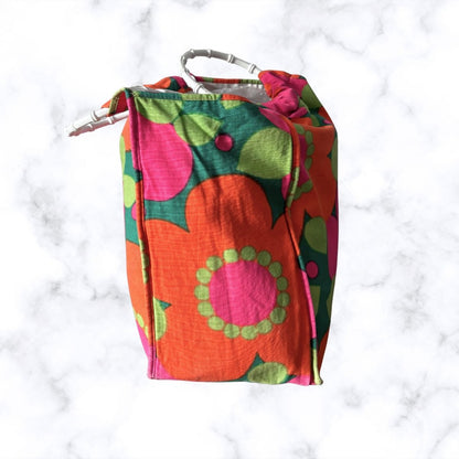 A vintage-style fabric storage bag with a retro floral pattern in orange, pink, green, and dark green, featuring a white plastic  handle, set against a white marble background.