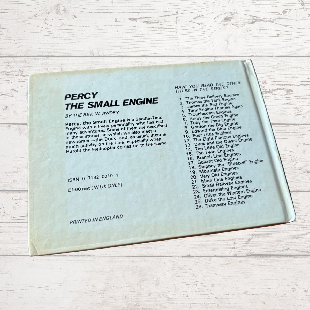 Back cover of a book titled 'Percy the Small Engine' with text on a light wooden surface.