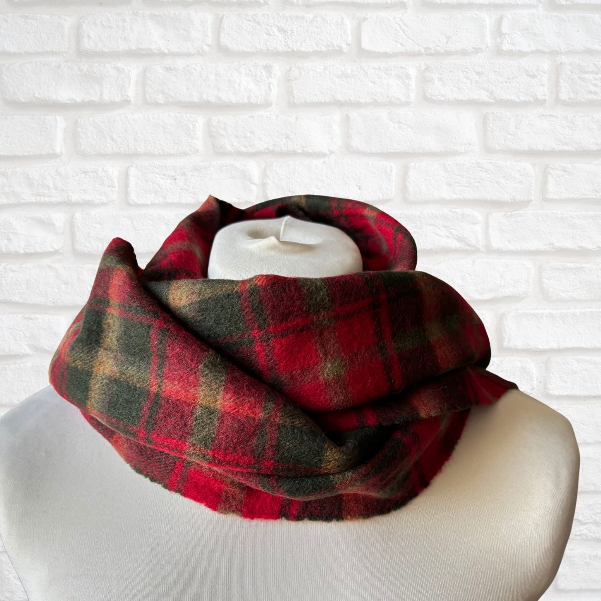 Red and green plaid scarf on a mannequin against a white brick wall background