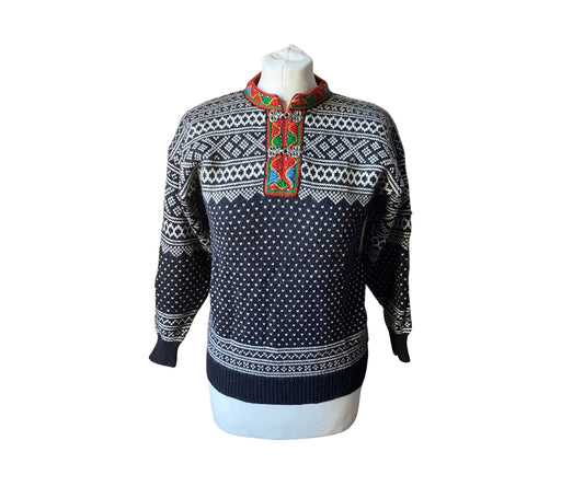 Black and white vintage jumper with red green and blue embroidery around the neckline and metal clasp fastening. 