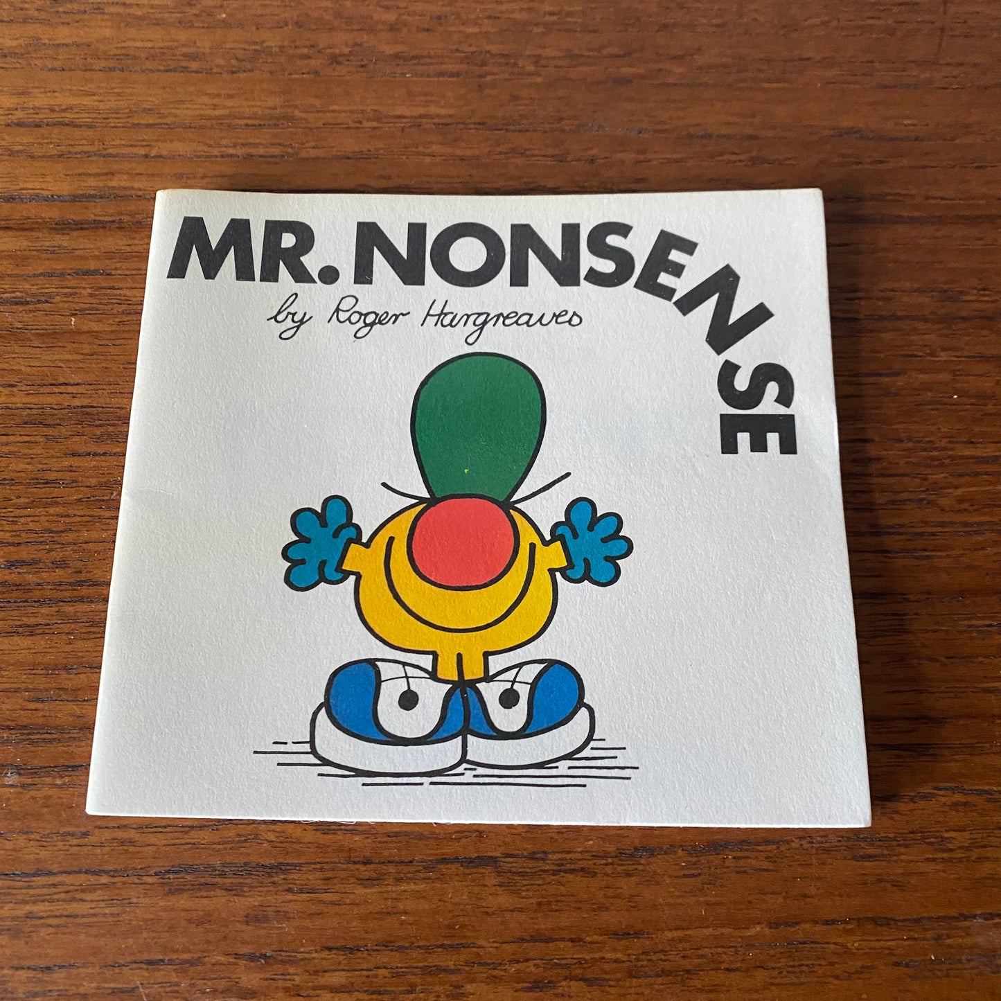 A small white vintage book. Mr Nonsense by Roger Hargreaves. Cover features of small yellow character with a big red nose, blue gloves and a large  green hat 